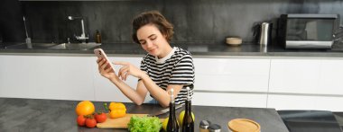 Mutfakta güzel esmer kadın portresi, yemek pişirme, akıllı telefon tarifi arama, yemek blogu için fotoğraf çekme, sebzelerden yemek pişirme, vejetaryen salatası..