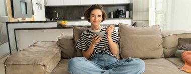 Modern kadın portresi, mısır gevreğini sütle yiyen ve kanepede oturan, TV karşısında dinlenen, evde kahvaltı yapan.