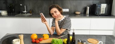 Mutfakta güzel esmer kadın portresi, yemek pişirme, akıllı telefon tarifi arama, yemek blogu için fotoğraf çekme, sebzelerden yemek pişirme, vejetaryen salatası..
