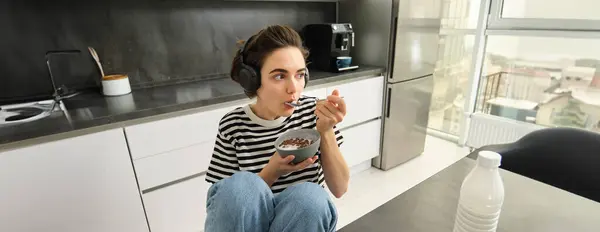 stock image Image of stylish, modern woman, student eating cereals with milk for breakfast, holding bowl and spoon, listening music in wireless black headphones.