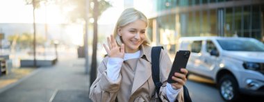 Sokaktaki mutlu, güzel genç bir kadın görüntüsü, video çağrılarına cevap veriyor, akıllı telefon kamerasına el sallıyor, merhaba diyor, mobil uygulama üzerinden arkadaşlarıyla konuşuyor, yol boyunca yürüyor..