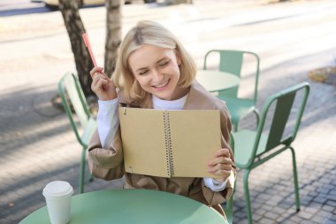 Genç, güzel sarışın bir kadının portresi, kafeteryada sanatsal bir kız, elinde defter ve kalem, günlüğüne yazıyor, dışarıda çizimler yapıyor..
