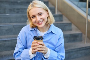 Kadın modelin yakın portresi, elinde kahve olan sevimli bir öğrenci, kampüsün yakınındaki merdivenlerde oturuyor, dışarıda vakit geçiriyor..