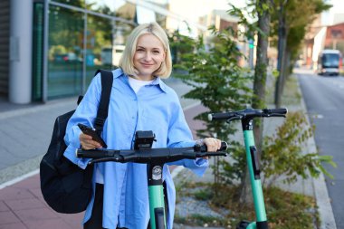 Paylaşılan Elektrikli Scooter 'ın gidonunda QR kodu taranıyor. Caddedeki Yeşil E-Scooter 'ın kilidini açan Kadın El Tutma Akıllı Telefonu' nu kapat.