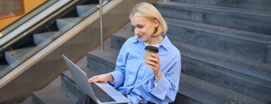 Genç bir kadın, mavi gömlekli bir öğrenci, dizüstü bilgisayarla çalışıyor, sokak merdivenlerinde oturuyor, internette proje üzerinde çalışıyor, halka açık kablosuz internete bağlanıyor, para kazanıyor..