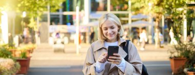 Genç, gülümseyen sarışın bir kadının portresini yakın çektir. Sokaktaki öğrenci, cep telefonu kullanıyor, akıllı telefondan mesajları kontrol ediyor, yolda yürüyor..