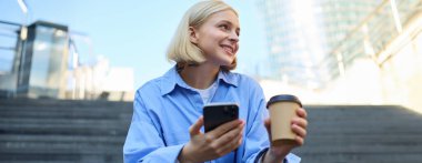 Gülümseyen, güzel, genç bir kadının hayat tarzı, kahve içen, cep telefonu kullanan, şehirde dinlenen, merdivenlerde oturan.