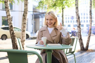 Gülümseyen mutlu kadın, kafede oturup başparmak kaldıran, kahve tavsiye eden, ona olumlu geri bildirim veren..