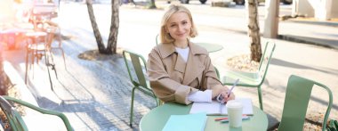 Gülümseyen genç bir kadının portresi, çalışan bir öğrenci dışarıda ödev yapıyor, sokak kafesinde oturuyor, kahve içiyor..