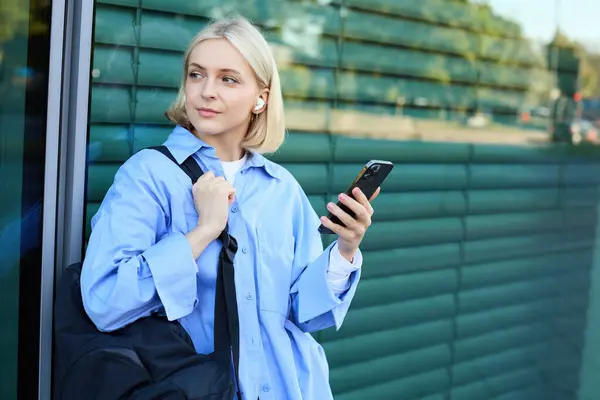 Sırt çantalı genç bir kız modelin hayat tarzı portresi. Sokakta bekleyen, akıllı telefonlu birini bekliyor..