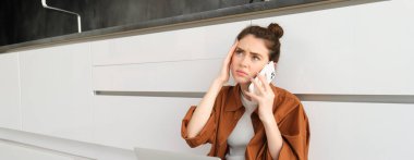 Doktorunu telefonla arayan, elinde akıllı telefon tutan, kaşlarını çatan ve kafasına dokunan bir kadının portresi, ağrılı bir baş ağrısı veya migreni var, kendini kötü hissediyor..
