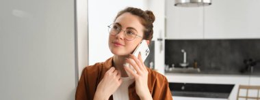 Evdeki mutlu kadın portresi, telefonlara cevap veriyor, cep telefonuyla konuşuyor, akıllı telefon tutuyor ve gülümsüyor..