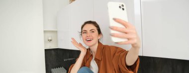 Hevesli tatlı kız mutfak tezgahında fotoğraf çekiyor, akıllı telefon uygulamasında selfie çekiyor..