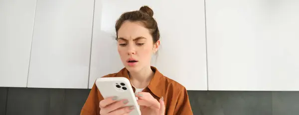 Portrait of woman with frowned face, looking at her mobile phone screen, scrolling social media feed, buying online, shopping on an app.
