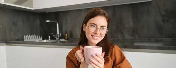 Woman drinking hot coffee at home. Thoughtful young woman drinking a cup of tea while thinking. Pretty girl with sweater relaxing at home while drinking purifying herbal tea.
