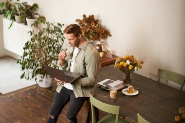 Genç yöneticinin portresi, masada oturan, dizüstü bilgisayarı tutan, ekrana odaklanmış görünen, proje bilgilerini okuyan, iş verilerini kontrol eden, ofiste çalışan ya da ortak çalışan.
