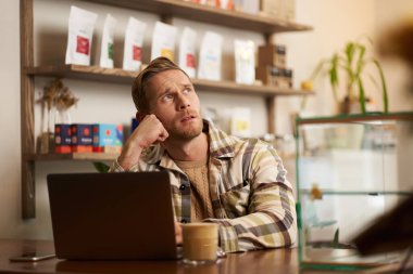 Bir kahve dükkanında uzaktan çalışırken konsantre olmuş gibi görünen bir adam. Kafe sahibi laptopuyla oturmuş, kapuçino içiyor, düşünceli bir yüz ifadesiyle yan gelip bakıyor, ilham alıyor..