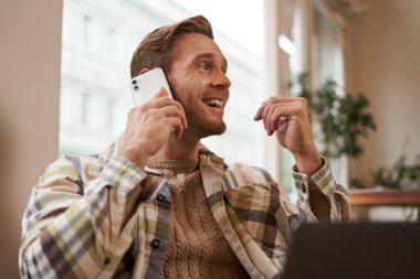 Genç işadamının portresi, şehirdeki kahve dükkanından uzaktan çalışan, dizüstü bilgisayarlı sandalyede oturan, bir telefona cevap veren, cep telefonuyla konuşan.