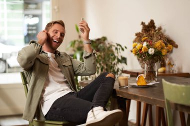 Kafedeki yakışıklı adam, kablosuz kulaklıkla müzik dinliyor, akıllı telefon çalma listesindeki favori şarkının tadını çıkarmak için kafeye bağlanıyor, oturup cappuccino içiyor..