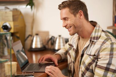 Yakışıklı iş adamının portresi, genç dijital göçebe, kafede oturuyor ve bilgisayarına bakıyor, uzaktan çalışıyor, kafeden bağımsız proje yapıyor..