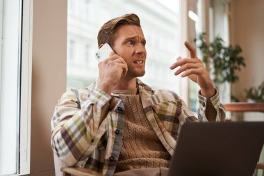 Telefonda konuşurken strese giren bir adamın görüntüsü. İş adamı laptopuyla kafede oturuyor, telefona cevap veriyor, telefondan kötü haberler alıyor..