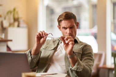 Yeni mavi ışık gözlüklü bir adamın portresi, bilgisayar ekranındaki lense bakıyor, kafede dizüstü bilgisayarla oturuyor ve gözlüğünü test ediyor..