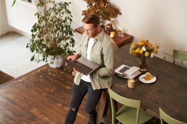 Genç bir adamın resmi, başarılı bir iş adamı masada oturuyor, dizüstü bilgisayara bakıyor, bir ofiste çalışıyor, projeye odaklanıyor, işini yapıyor, kahve içiyor..
