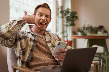 Yakışıklı erkek kafe ziyaretçisinin portresi, dizüstü bilgisayarda çalışan iş adamı, akıllı telefon tutan, cep telefonu işareti gösteren, beni ara..