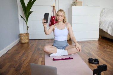 Güzel bir yaşam tarzı blogcusunun portresi, kendini evde çalışırken kaydetmek, odasında yoga yapmak, akıllı telefondan selfie çekmek, dijital video kamera kullanmak..