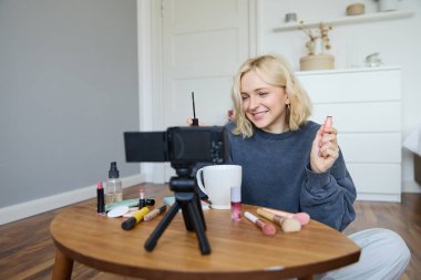 Sarışın, gülümseyen bir kadının portresi, sosyal medya için video kaydeden, rimel tutan, takipçileri için güzellik ürünlerini yorumlayan bir yaşam tarzı blogu, vlogger veya makyaj sanatçısı kaydeder..