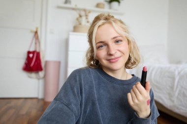 Genç makyaj sanatçısının portresi, güzellik blogcusu yeni ruj gösteriyor, odasında video kaydediyor, gülümsüyor ve pozitifliğini ifade ediyor..