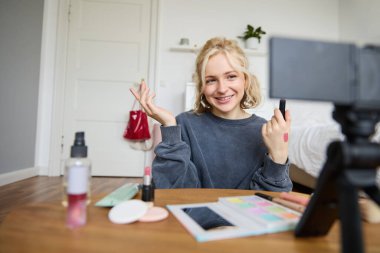 Genç ve şık bir kadının görüntüsü, blogcu en iyi rujunu seçerken, teninde dudak kremi örneklerini gösterirken, boş bir odada dijital kameranın önünde otururken güzellik videosu kaydediyor..