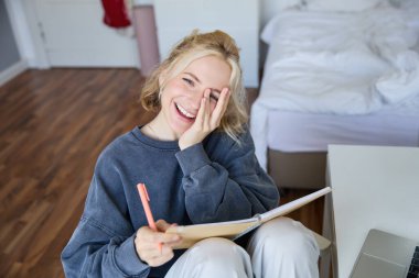 Mutlu, genç sarışın bir kadının portresi, yatak odasında defter ve kalemle oturuyor, gülüyor ve gülümsüyor, günlüğe yazıyor, ödev yapıyor ve gülümsüyor..