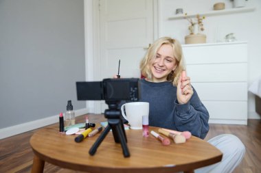 Neşeli, genç ve güzel bir blog yazarı, yerde oturup makyaj hakkında video kaydeden, rimel tutan, sosyal medya hesabı ve takipçileri için yaşam tarzı içeriği sağlayan bir kadın..