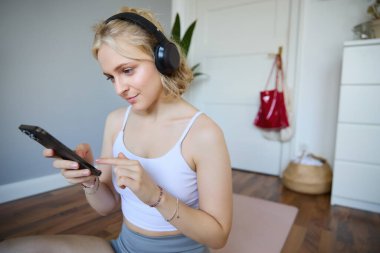 Fitness Podcast 'i seçen sarışın genç kadının portresini yakından çek, cep telefonuna bak, akıllı telefondan egzersiz uygulamasına bak, kablosuz kulaklık tak,.