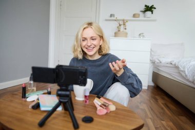 Odasında genç bir kızın portresi, günlük bir video kaydı, sosyal medya için günlük bir yaşam tarzı videosu, internetteki internet etkileyicisi reklam ürünü, kamerayla konuşmak, yerde oturmak..
