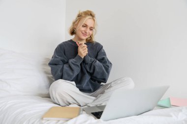 Yatakta dizüstü bilgisayar ve defterlerle oturan, evden çalışan, serbest çalışan güzel bir kadının portresi. İnternette okuyan kız öğrenci, görüntülü sohbetler, derslere uzaktan bağlanıyor..