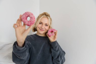 Güzel sarışın kadın portresi, iki pembe çörek, lezzetli pasta, tatlı yemek ve gülümsemek, seninle yemek paylaşmak..