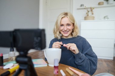 Sarışın, gülümseyen bir kadının portresi, sosyal medya için video kaydeden, rimel tutan, takipçileri için güzellik ürünlerini yorumlayan bir yaşam tarzı blogu, vlogger veya makyaj sanatçısı kaydeder..
