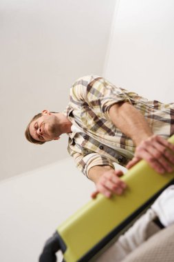 Çantayı kapatmaya çalışan komik bir adam resmi. Elbise yığını, bavul, eşyaları çantaya koyuyor. Turizm ve gezgin konsepti