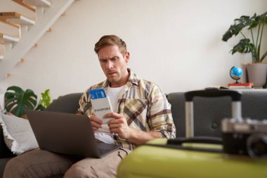 Huysuz adamın portresi, elinde biletler ve pasaport, dizüstü bilgisayar açıldı, endişeli ve sinirli görünüyor, bavuluyla koltukta oturuyor..