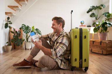 Yakışıklı genç bir adamın portresi, bavuluyla oturan bir turist, elinde pasaport ve uçak biletleri, tatile çıkıyor..