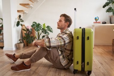 Yakışıklı genç bir adamın portresi, bavuluyla oturan bir turist, elinde pasaport ve uçak biletleri, tatile çıkıyor..