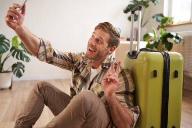 Elinde bavulla gülümseyen yakışıklı bir adamın portresi, bavulla selfie çekmesi, sosyal medyada tatile çıkmakla ilgili yazılar yazması. Turizm ve blog kavramı