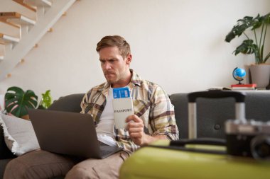 Sinirli adam uçak biletlerini tutuyor, dizüstü bilgisayara bakıyor, tatil turunda sorun yaşıyor..