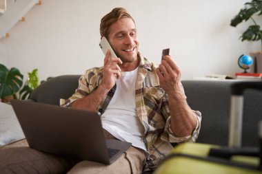 Gülümseyen adamın portresi, turist rezervasyon oteli, telefondan onay, kredi kartı ve dizüstü bilgisayar..