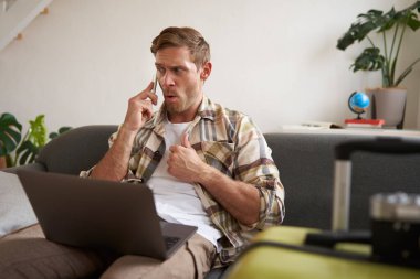 Kızgın bir adamın portresi, hayal kırıklığına uğramış gibi görünüyor, cep telefonuyla konuşuyor, dizüstü bilgisayar ve bavulla oturuyor. Turizm ve halk konsepti