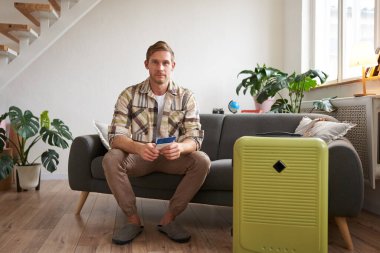 Yakışıklı bir gencin portresi, uçak biletleri, tatile gitmek, bavulla koltukta oturmak, havaalanına gitmek için taksi beklemek. Boşluğu kopyala