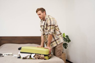 Genç bir adamın portresi, gezgin tatile çıkıyor, bavulunu ütülüyor, iç çamaşırlarını itmeye çalışıyor, bavullarını kapatıyor, tatil için bir sürü şey hazırlamaya çalışıyor. Turizm konsepti