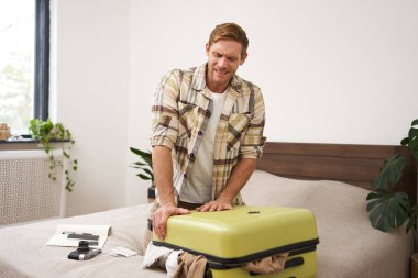 Genç bir yolcunun görüntüsü, bavulunu kapatmaya çalışan bir turist, onu kapatmak için bavulları itiyor, tatilde bir sürü kıyafet taşıyor. Boşluğu kopyala